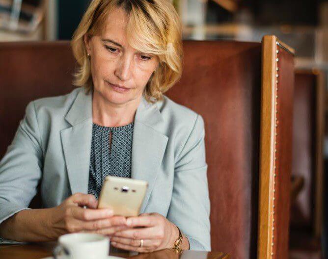 woman sitting at booth with coffee looking at her phone